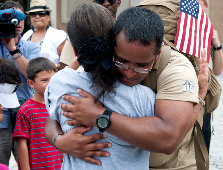 Emotional reunion of a soldier and loved one hugging in a crowded public setting.