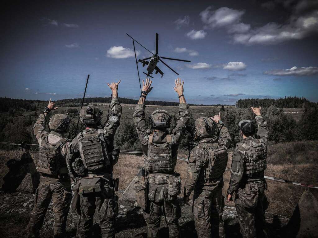Soldiers waving at a helicopter during a military field operation.