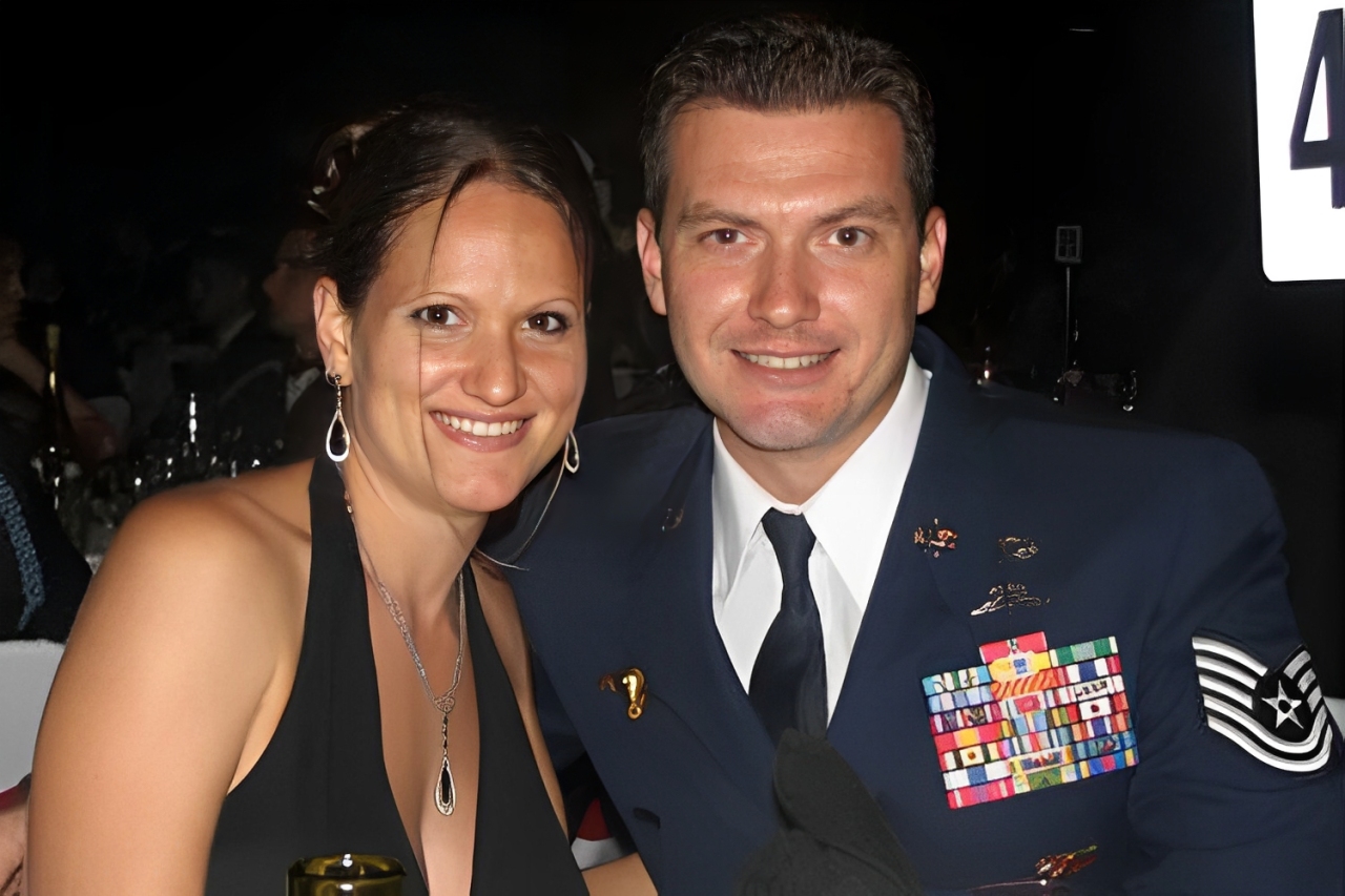 Smiling couple at a formal event, with the man in a decorated military uniform.