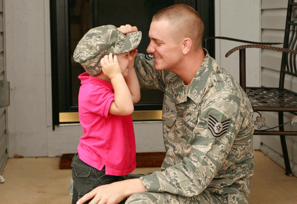 Military father smiling as his young child wears his cap.
